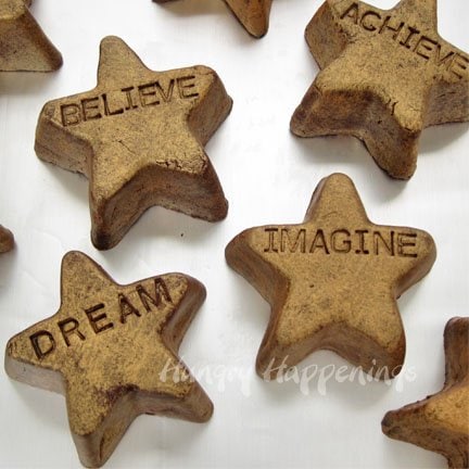 dark chocolate fudge stars decorated with gold spray and imprinted with sayings including "believe," "imagine," "dream," "achieve," and more. 