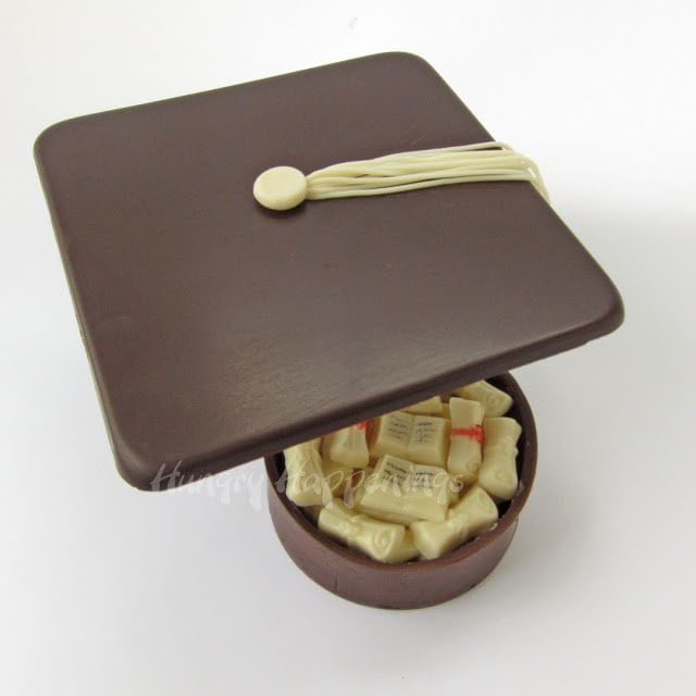 chocolate box lid set askew showing the graduation chocolates inside the round chocolate box. 
