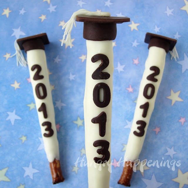 White chocolate dipped pretzels decorated for a graduation party with a grad cap and date.