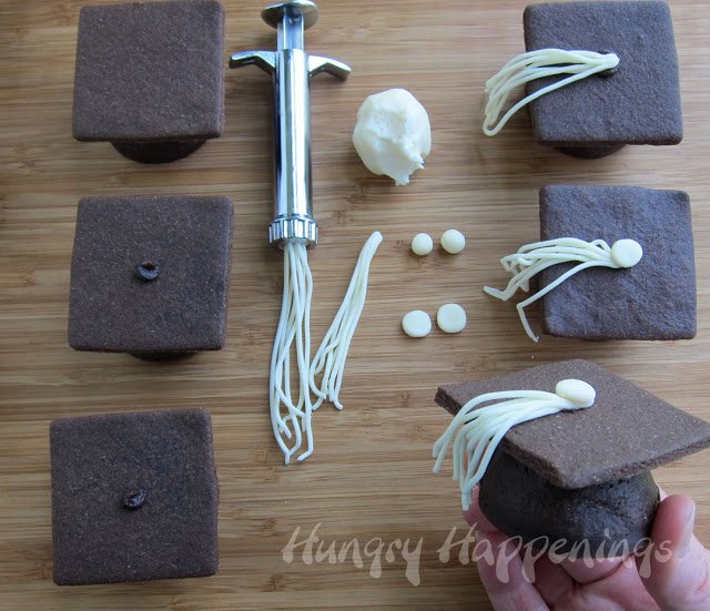 adding white modeling chocolate tassels to the 3-D chocolate graduation cookies
