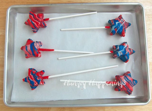 Six red white and blue rice crispy treats star lollipops on a parchment paper lined baking tray.