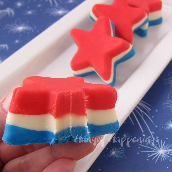 a bite taken out of one red, white, and blue fudge star with others on a serving platter set on blue fireworks scrapbooking paper. 