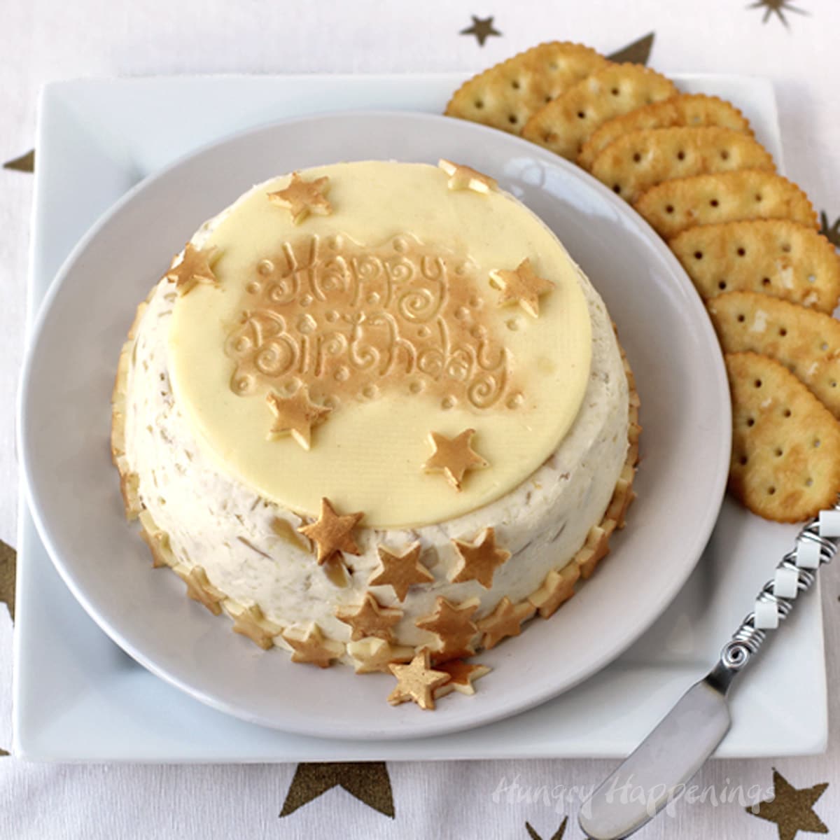 Elegant birthday cake cheese ball topped with gold-colored cheese stars and a "happy birthday" topper.