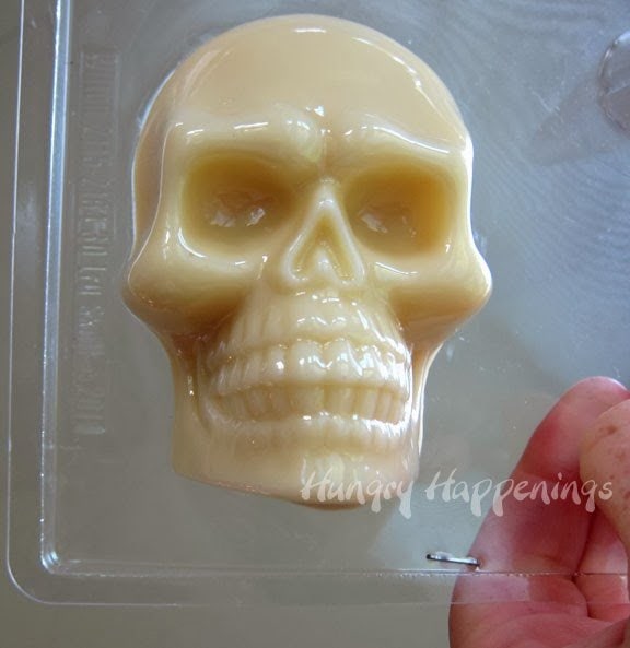 the front view of a plastic skull mold filled with melted white cheese. 