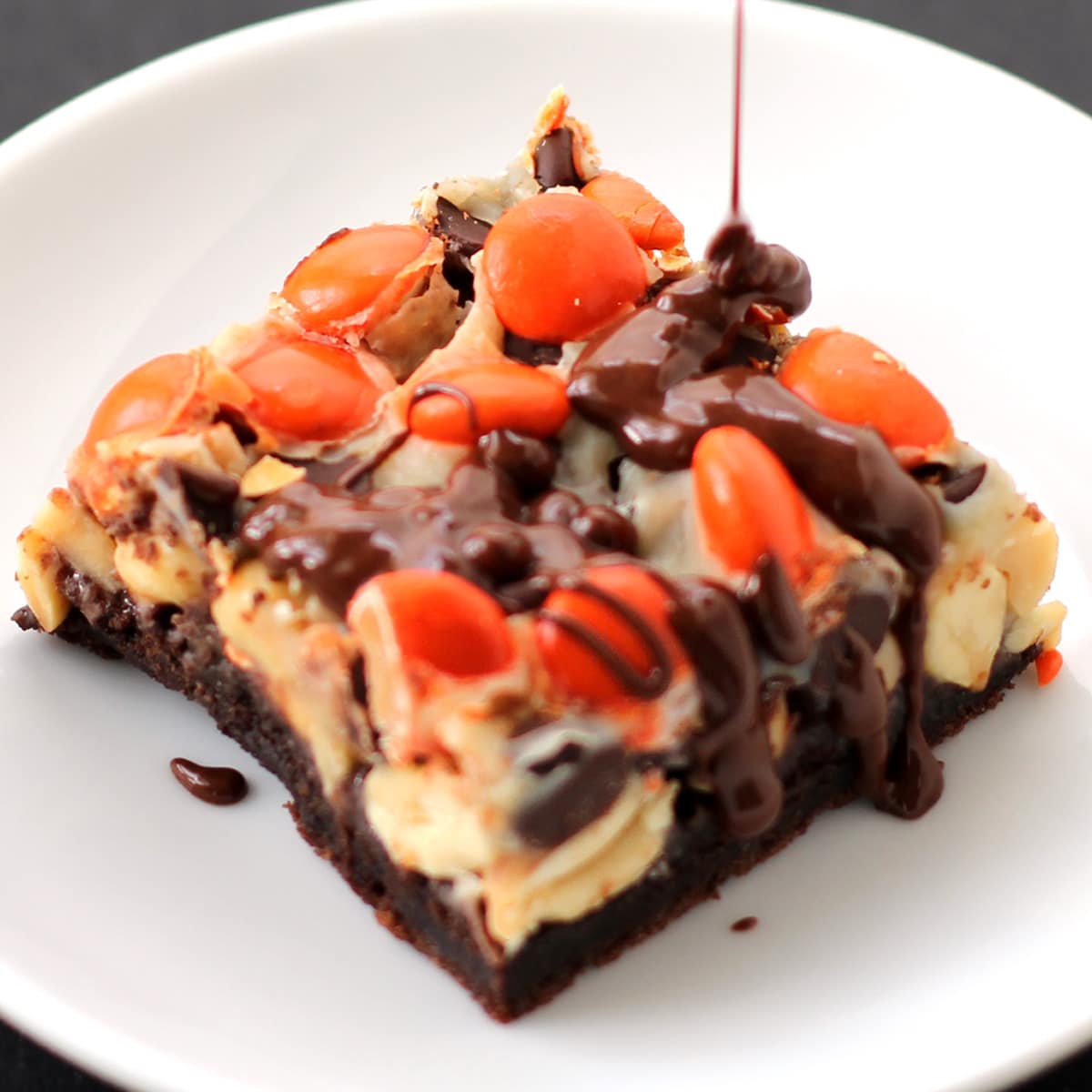 Drizzling chocolate peanut butter glaze over Reese's pieces topped magic bars.