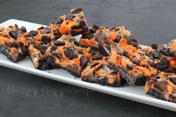 Halloween Magic Bars are stacked up on a long white plate set on a grey background