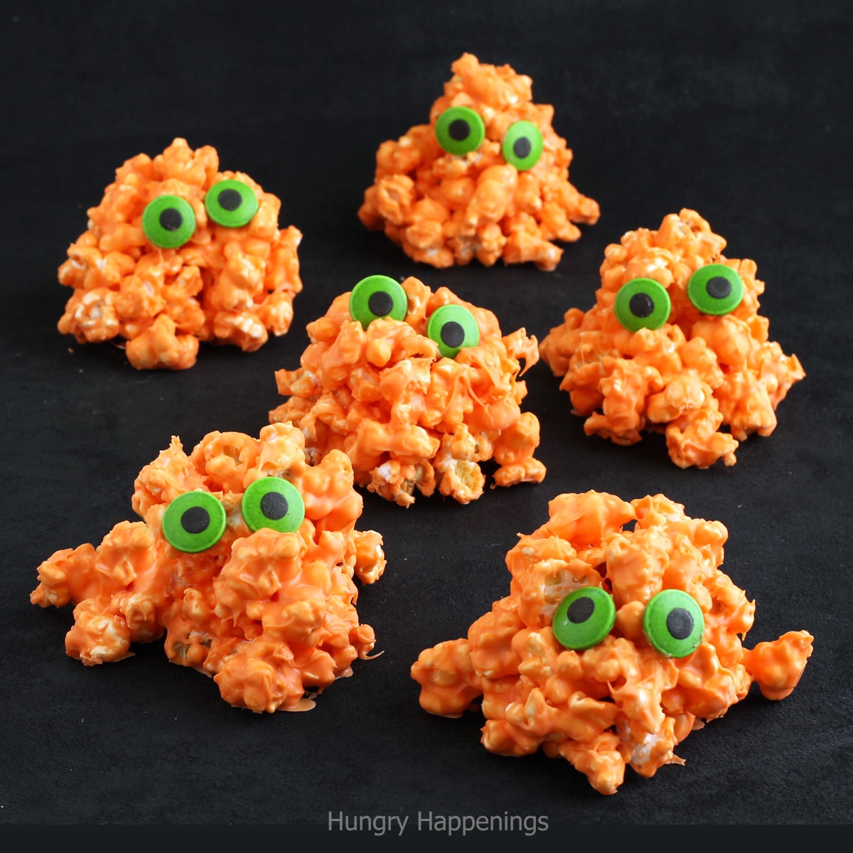 popcorn monsters made with orange-colored white chocolate popcorn and green candy eyes.