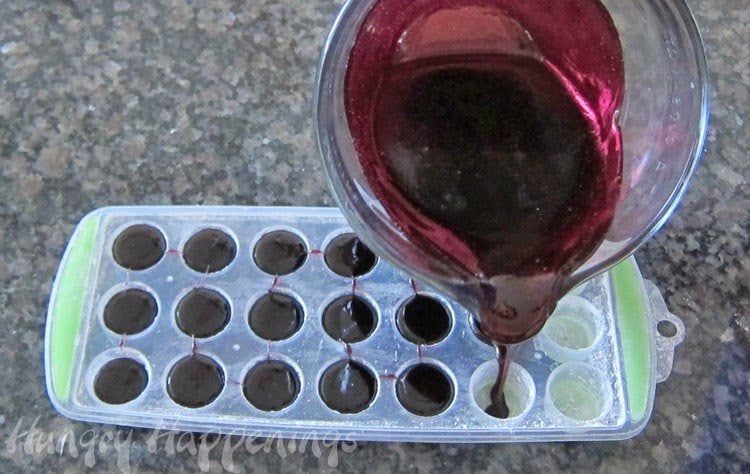 pouring blueberry gumdrop syrup into an ice cube tray.
