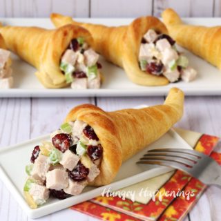crescent roll cornucopia filled with cranberry turkey salad on a plate set next to a fork and Thanksgiving napkin