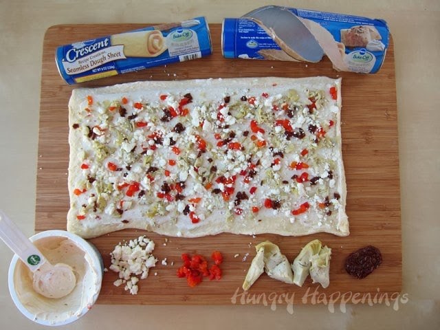 spread cream cheese over the crescent roll dough sheet then top with feta cheese, roasted red peppers, artichokes, and sun-dried tomatoes
