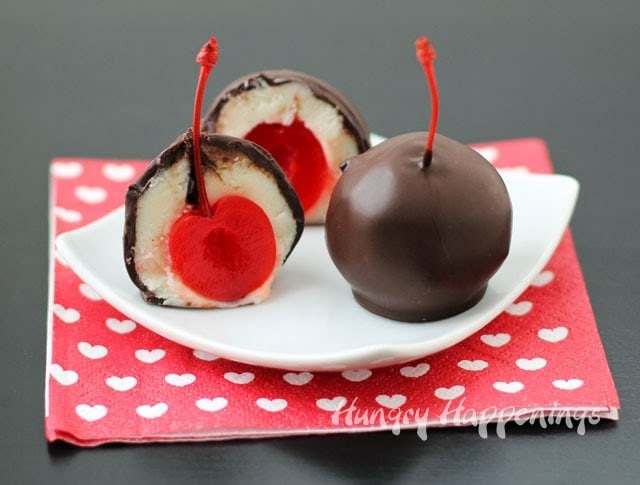 chocolate-dipped white cake balls filled with maraschino cherries served on a white square plate on a red and white heart napkin.