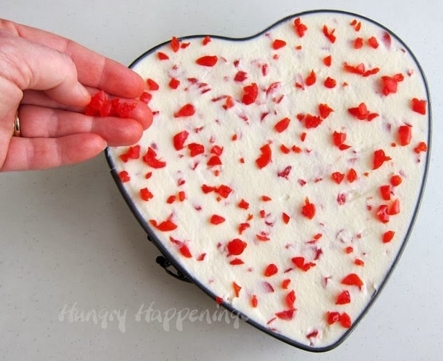 adding chopped maraschino cherries on top of a triple layer chocolate mousse cake heart