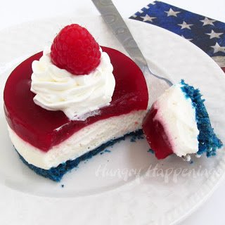 Red, white, and blue no-bake cheesecake topped with whipped cream and a raspberry