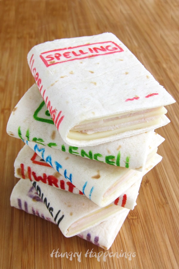 A stack of mini sandwich school books made using soft flour tortillas, ham, cheese, and food coloring. 