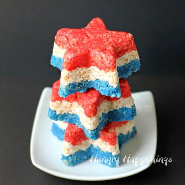 3 Rice Krispie Treat Stars with layers of red, white, and blue marshmallow crispy treats stacked up on a small square white plate.