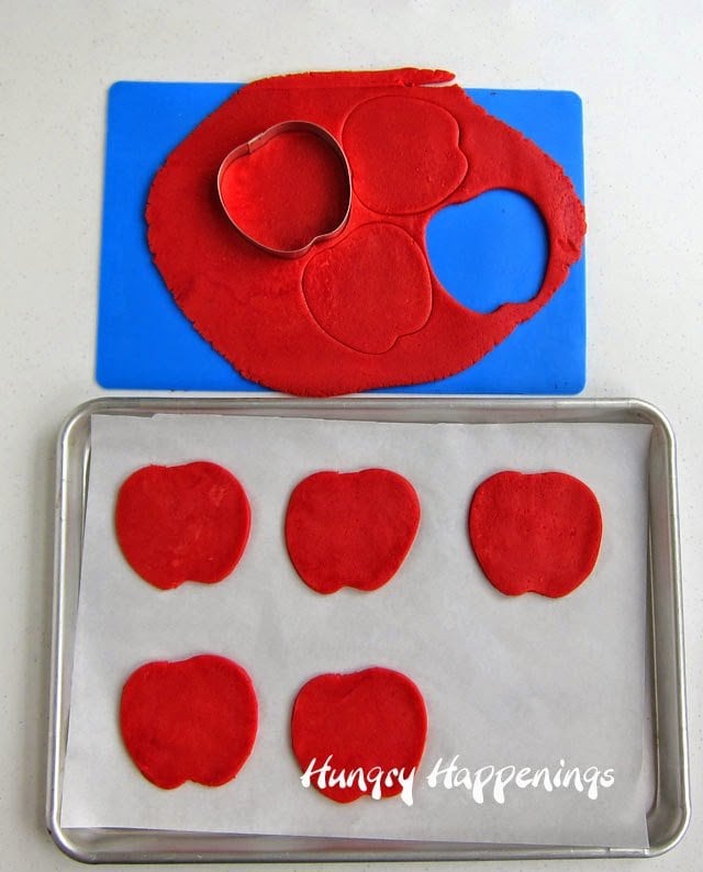 cutting out red cookie dough using an apple cookie cutter.