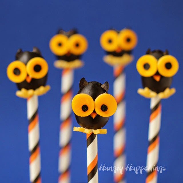 five black olive owls with orange cheese eyes and feet and carrot beaks on striped paper straws