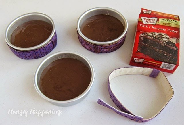 Duncan Hines chocolate fudge cake batter divided into three 6-inch round cake pans surrounded by cake strips. 