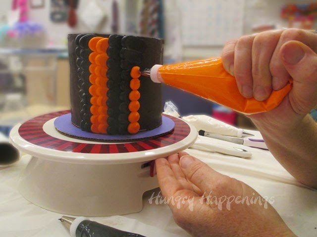adding rows of orange dots and petals along with black dots and petals on a chocolate cake. 