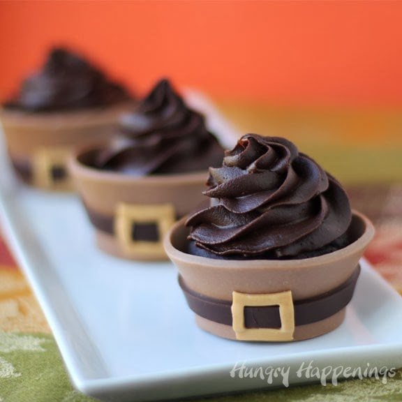 chocolate cupcakes wrapped in modeling chocolate pilgrim suits are topped with a big swirl of chocolate ganache frosting