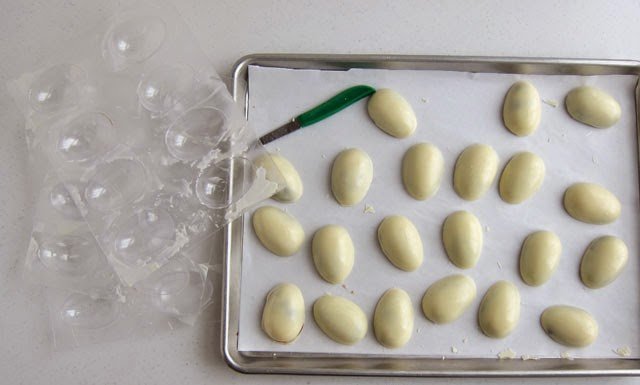 white chocolate eggs on a parchment paper-lined baking sheet next to egg candy molds. 