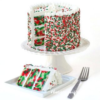 Christmas cake covered in red and green sprinkles with slices of red, white, and green tie-dye cake layered with vanilla frosting. 
