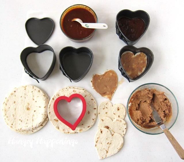 cut tortilla hearts, top with refried beans. and layer on enchilada sauce in heart-shaped springform pan