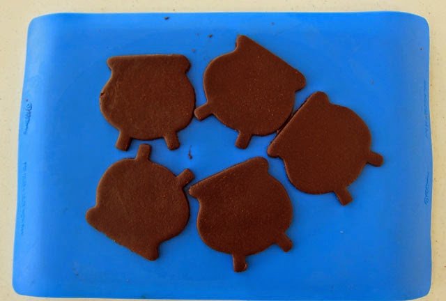 chocolate pot of gold (cauldron) cookies cut out on a blue silicone mat