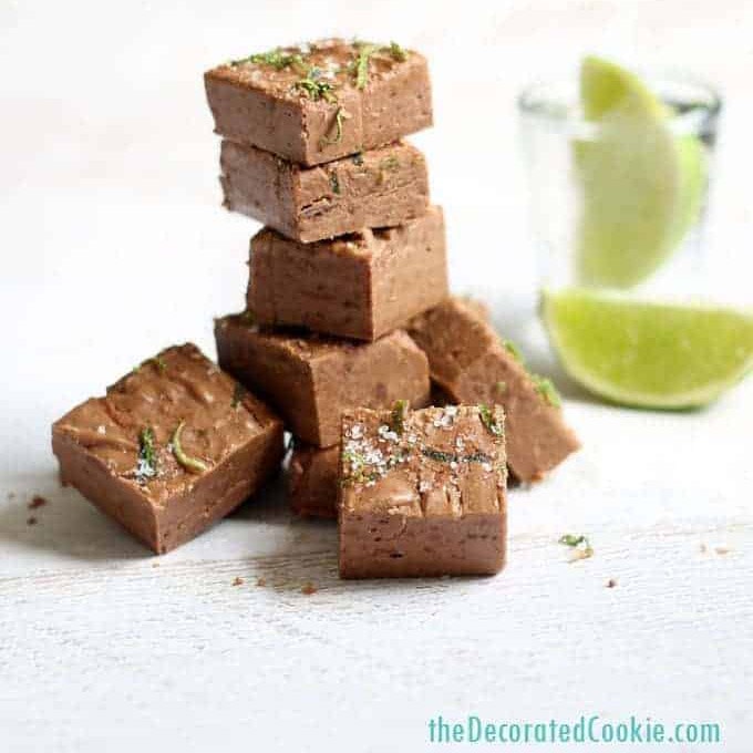 tequila fudge topped with lime zest stacked in front of a glass of tequila with lime wedges.