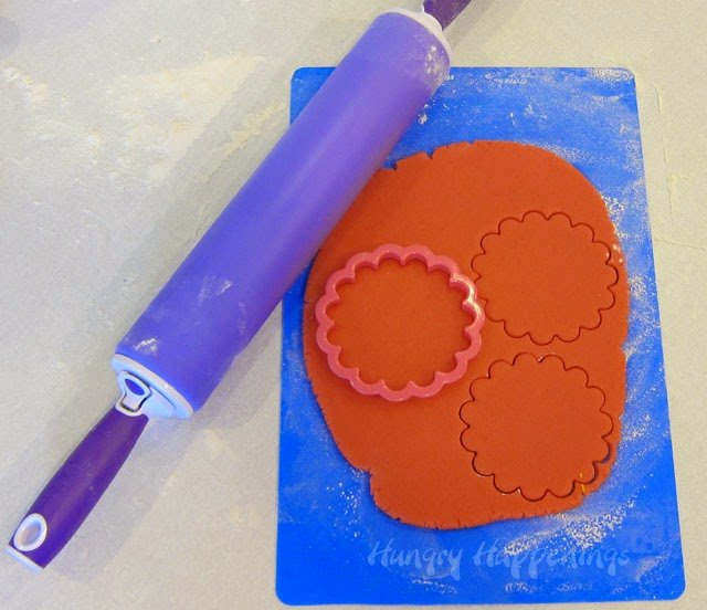 rolling out pink cookie dough and cutting out the flower-shaped bases for the hat cookies