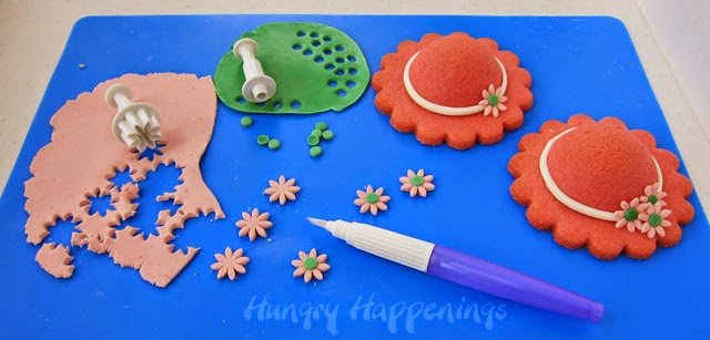 cutting out pink daisies and green dots out of modeling chocolate and attaching them to the hat cookies.