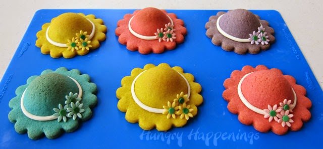 decorated yellow, pink, purple, and blue hat cookies set on a blue silicone mat