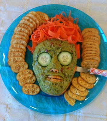 guacamole covered face-shaped cheese ball with orange carrot hair. 