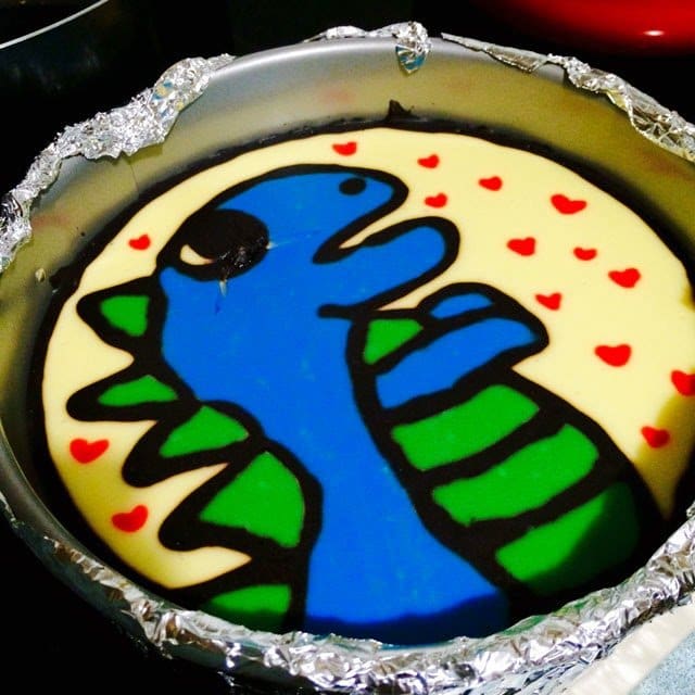 cheesecake decorated with a blue and green dinosaur. 