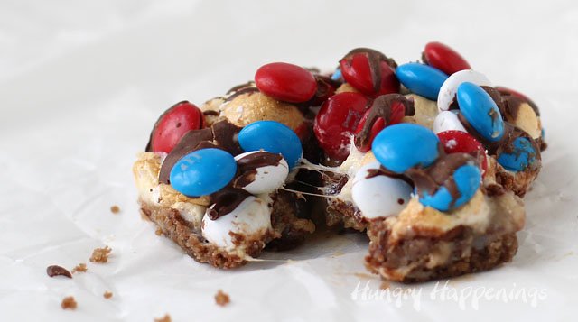 Go ahead, take a bite. These S'mores Magic Bars are layers with S'mores Oreos, melted chocolate, crunchy graham crackers, gooey caramel, toasted marshmallows and M&M's. Recipe from HungryHappenings.com
