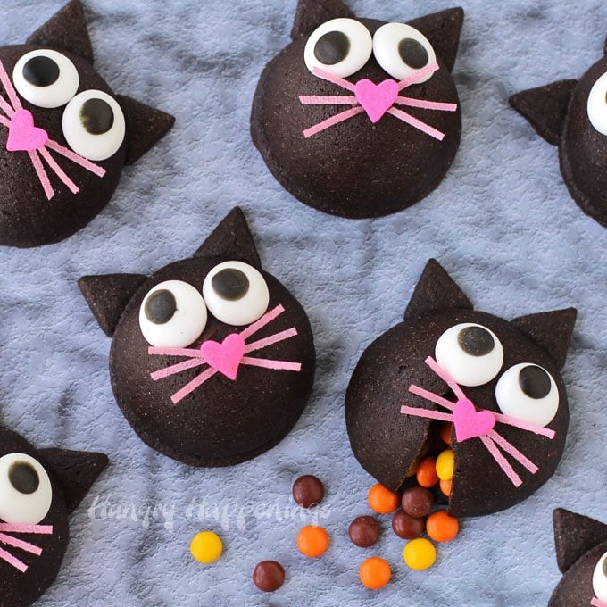 black cat cookies filled with candy have big candy eyes, pink heart-shaped nose sprinkles and pink whiskers.
