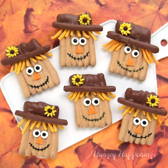 peanut butter and milk chocolate dipped pretzel sticks decorated with modeling chocolate to look like scarecrows