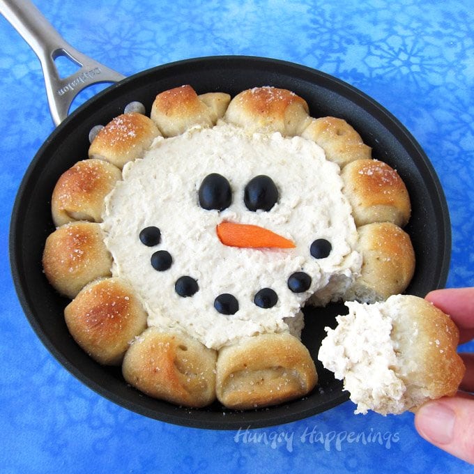 skillet dip snowman with bread puffs surrounding hot chicken dip decorated with black olives and a carrot nose