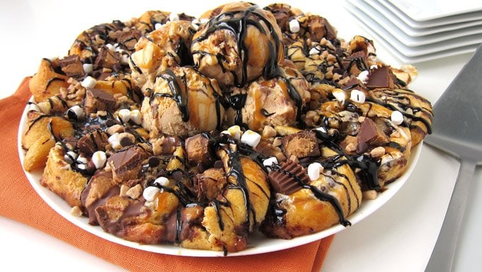 Ooey Gooey Crescent Ring Dessert topped with peanut butter cheesecake mousse, melted chocolate, gooey marshmallows, peanut butter cups, toffee bits, hot fudge, and caramel sauce, all served with salted caramel ice cream.
