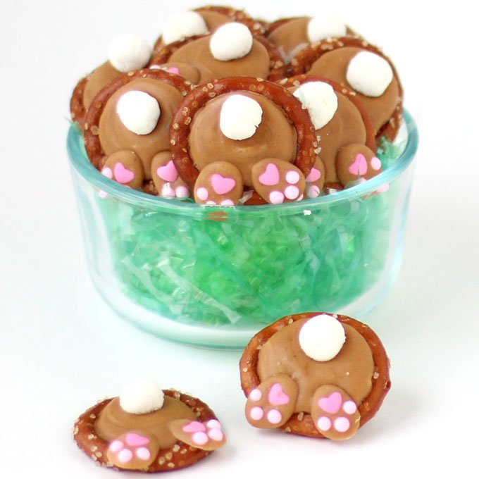 Peanut Butter Bunny Butt Pretzels in a clear glass bowl filled with green Easter grass. 