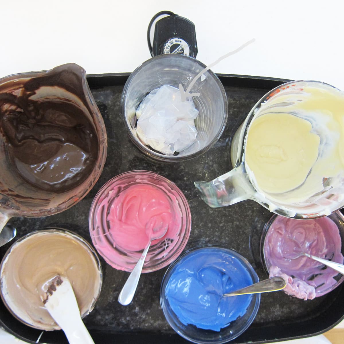 melting chocolate, pink, white, blue, purple, and tan candy melts in a water batch in an electric skillet. 