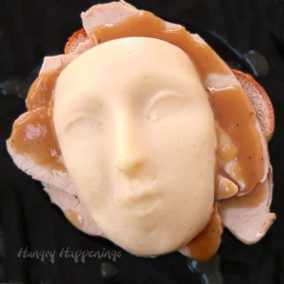 Mashed potatoes form an eerie face that sit atop a gravy covered turkey sandwich in this clever take on an open face sandwich. This is the perfect meal for your gory Halloween dinner.