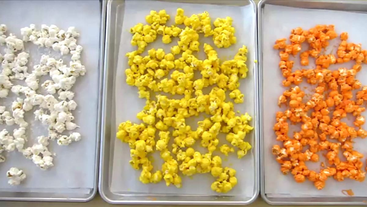 white, yellow, and orange popcorn on parchment paper-lined baking sheets. 