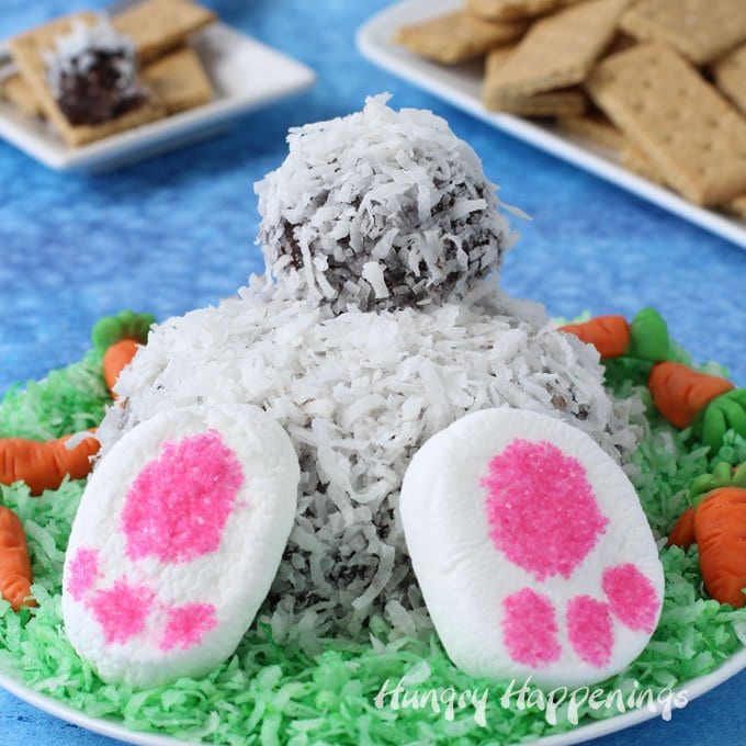  Chocolate Coconut Cheese Ball Bunny Bum served on a platter filled with green colored coconut with candy carrots and graham crackers.