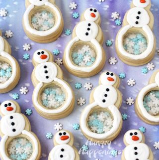 white chocolate topped snowman cookies have clear candy bellies and are filled with blue and white snowflake sprinkles