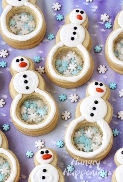 Cute snowman-shaped Christmas cookies decorated with white chocolate, snowflake sprinkles, black sugar peals, and orange chocolate-coated sunflower seeds.