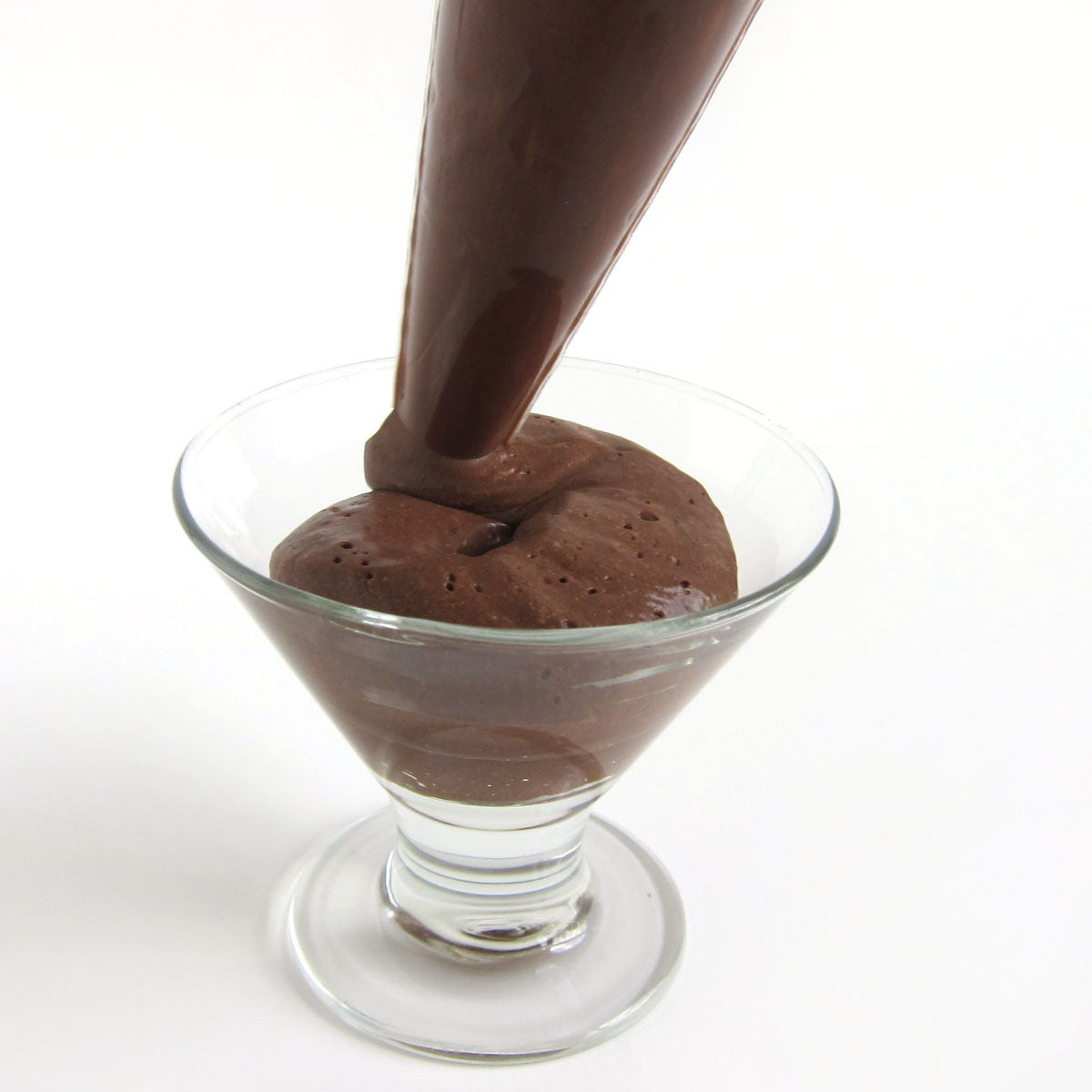 piping dark chocolate mousse into a small glass dessert cup