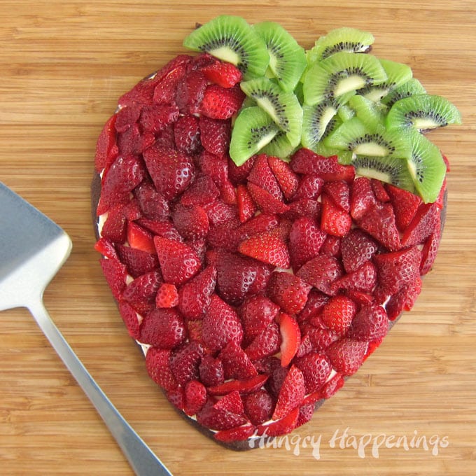 Strawberry shaped fruit pizza topped with fresh strawberries and kiwi on a cheesecake topped chocolate cookie.