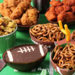 football party tablescape featuring a chocolate dip football, mini pretzel twists, chicken strips, and buffalo chicken nuggets