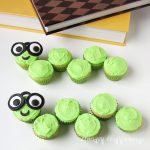 mini cupcakes frosted with bright green buttercream and arranged to look like bookworms with candy clay glasses and googly eyes sitting next to books